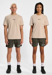 Beige sportshirts met korte mouwen van textuurstof, gecombineerd met donkergroene shorts waarop de tekst "ATW" aan de voorkant staat. Zwarte schoeisel weergegeven.