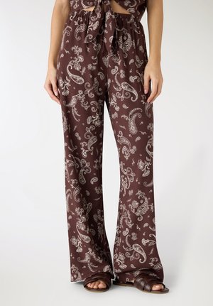 Pantaloni marroni a gamba larga con stampa paisley bianca, indossati con sandali marroni e un top corto annodato coordinato.