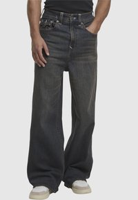 Granatowe dżinsy o szerokich nogawkach z wyblakłą tekstur�ą, pięcioma kieszeniami, kontrastowym przeszyciem i zapinaniem na guzik w pasie.