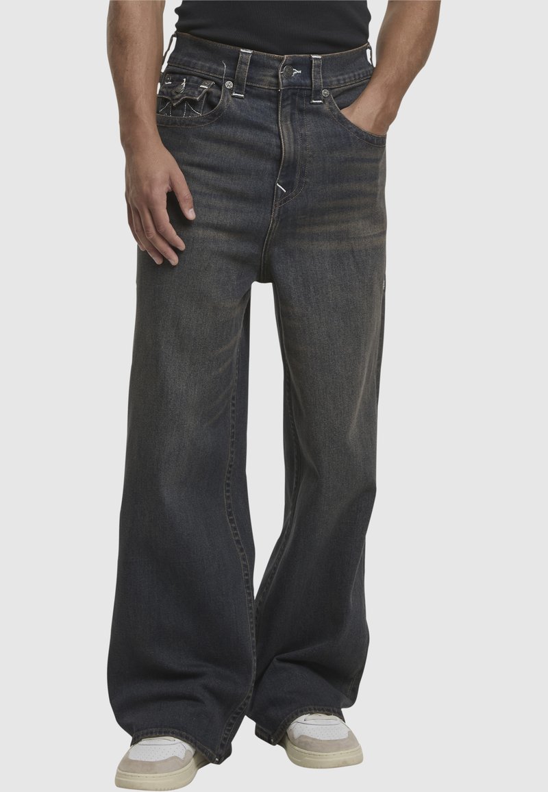Granatowe dżinsy o szerokich nogawkach z wyblakłą teksturą, pięcioma kieszeniami, kontrastowym przeszyciem i zapinaniem na guzik w pasie.