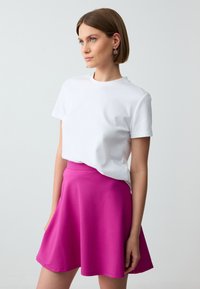 T-shirt bianco in cotone a maniche corte, abbinato a una gonna a ruota fucsia, lunga fino al ginocchio, realizzata in tessuto liscio e elastico.