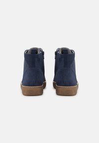 Navy blue suede ankle boots with a smooth texture, featuring a brown rubber sole and a green accent near the heel. Side zip closure.