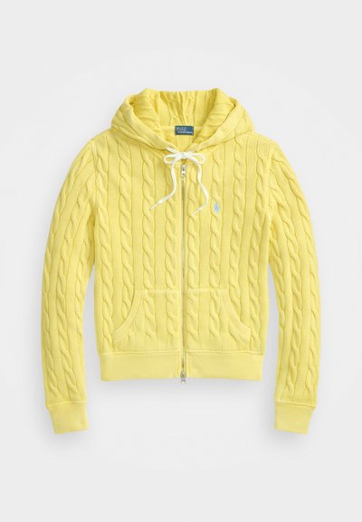 Rumena pletena kapuca z zadrgo spredaj, kapuco na vrvico in sprednjimi žepi. Vsebuje majhen modri logotip na levi strani prsnega dela.