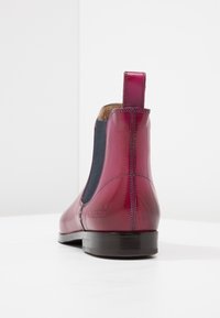 Lesklá tmavě červená kožená kotníková bota s černým elastickým bočním panelem, poutkem na zadní straně a nízkým černým podpatkem na bílé ploše.