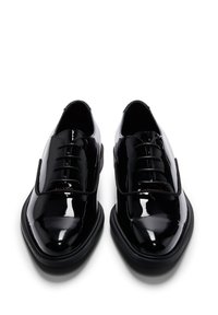 Chaussures noires en cuir verni avec un bout pointu, un laçage et une texture lisse. Présentent des coutures minimalistes et une semelle noire unie.