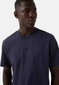 Mørkeblå bomulds T-shirt med rund hals, korte ærmer og et diskret tonal logo på brystet. Glat tekstur, almindelig pasform.