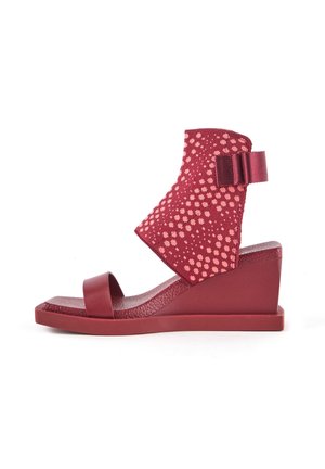 Czerwone sandały na wedgesie z teksturowanym wierzchem z tkaniny w kropki, z otwartym palcem i paskiem wokół kostki z tkaninowym akcentem w postaci kokardy.