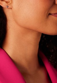 Zilveren studoorbellen met drie cirkelvormige elementen, met een glanzende afwerking. Draagt ze een model met krullend haar, gekleed in een roze kledingstuk.