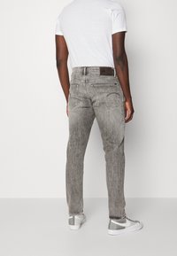 Jeans de mezclilla gris con un acabado desgastado, que cuentan con dos bolsillos traseros y un parche de cuero en la cinturilla. Combinados con zapatillas blancas.