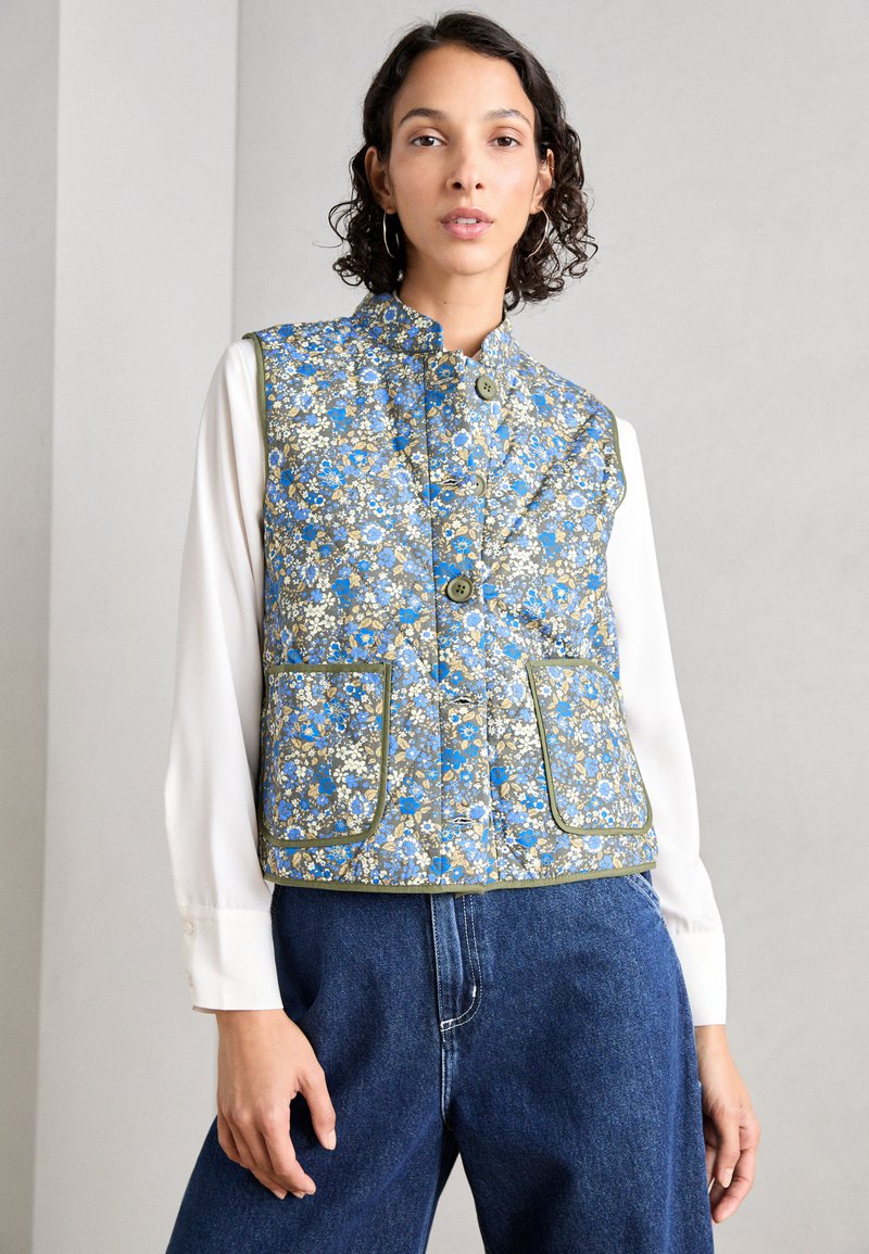 Κοντό γιλέκο με ανθισμένο σχέδιο σε μπλε, λευκό και ελιά, που διαθέτει μανταρίνι γιακά, μπροστινές τσέπες και κλείσιμο με κουμπιά.