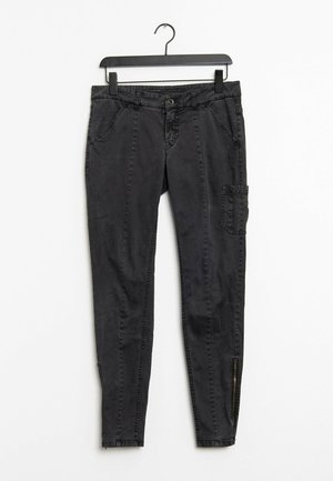 Zwarte slim-fit broek met voorzakken, een zijcargo zak en ritsen bij de enkelboorden, hangend aan een zwarte hanger tegen een witte achtergrond.