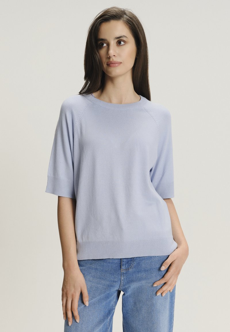Maglione corto a maniche corte di colore azzurro chiaro con scollatura rotonda, orlo a costine e cuciture laterali. Abbinato a jeans in denim azzurro chiaro.