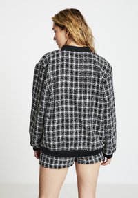 Black and white patterned bomber jacket with a ribbed collar and cuffs, featuring a textured woven fabric and coordinating shorts.