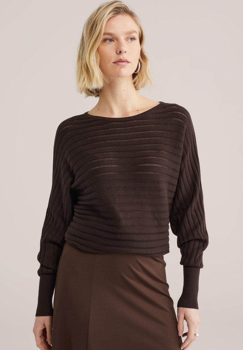 Pull en tricot marron avec des rayures horizontales, un large col et des manches bouffantes. La texture lisse complète une jupe marron ajustée.