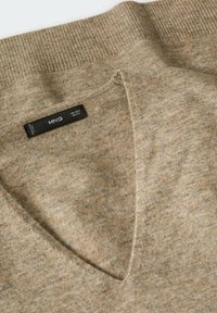 Pull en tricot marron clair avec encolure en V et bordure côtelée. Dispose d'une étiquette cousue avec "MNG" et des instructions de lavage. Texture douce.