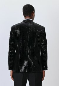Black velvet jacket with vertical sequined stripes. Features a peak lapel, single-button closure, and structured shoulders. Back view.