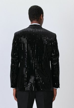 Black velvet jacket with vertical sequined stripes. Features a peak lapel, single-button closure, and structured shoulders. Back view.