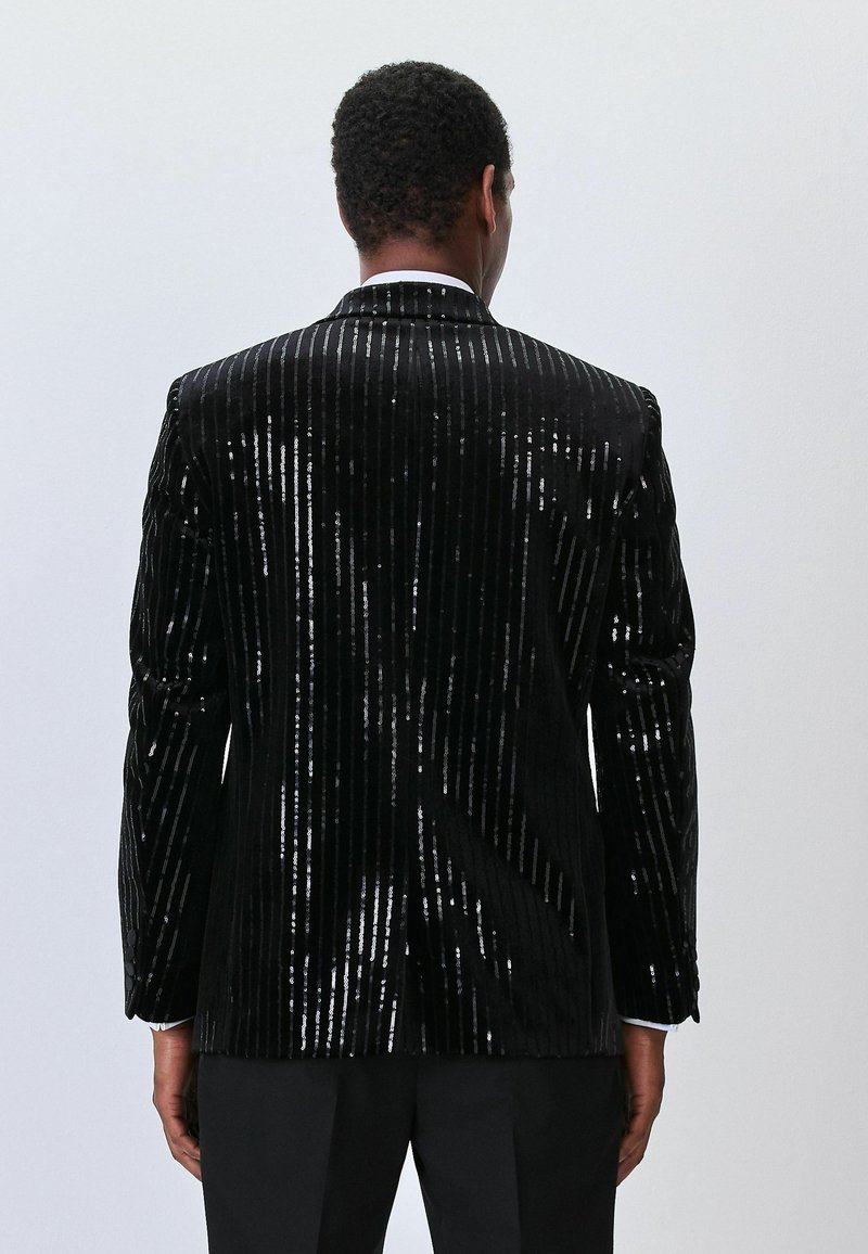 Black velvet jacket with vertical sequined stripes. Features a peak lapel, single-button closure, and structured shoulders. Back view.