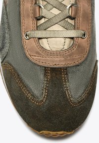 Zapatilla gris oscuro con parte superior de lienzo y detalles de cuero marrón, cordones redondos y suela de goma texturizada. Se puede ver el detalle de costura.
