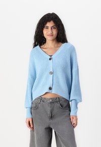 lichtblauwe cropped cardigan met een V-hals, geribde textuur en drie grote knopen aan de voorkant. Heeft losse mouwen en een boxy ontwerp.