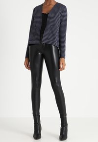 Marinrandig cardigan med avslappnad passform, kombinerad med svarta läderliknande leggings. Outfiten kompletteras med svarta klackstövletter.