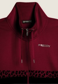 Giacca zip-up bordeaux con colletto alto, cordini, logo metallico "FREDDY" sul petto e dettaglio a stampa leopardata vicino all'orlo.