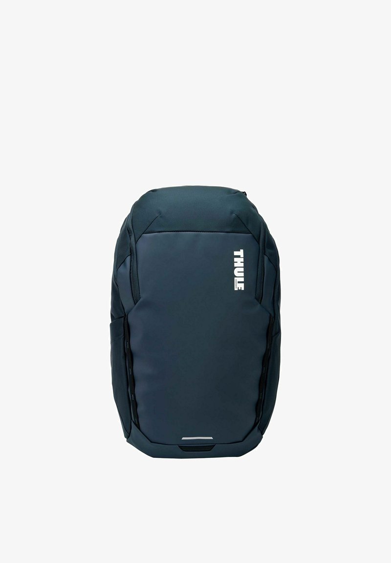 Sac à dos Thule bleu foncé au design élégant et profilé avec un logo blanc vertical sur le devant, comprenant des sections rembourrées et des poches latérales.