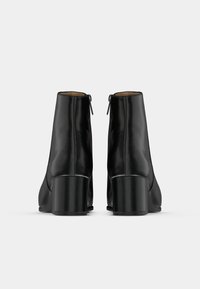 Černé kožené kotníkové boty s hladkým povrchem, zaoblenou špičkou a masivním podpatkem. Na zadní straně je nenápadný zip pro snadné obouvání.