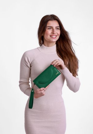 Green textured wallet with a circular design, gold hardware accents, and a detachable strap, held in a hand against a plain background.
