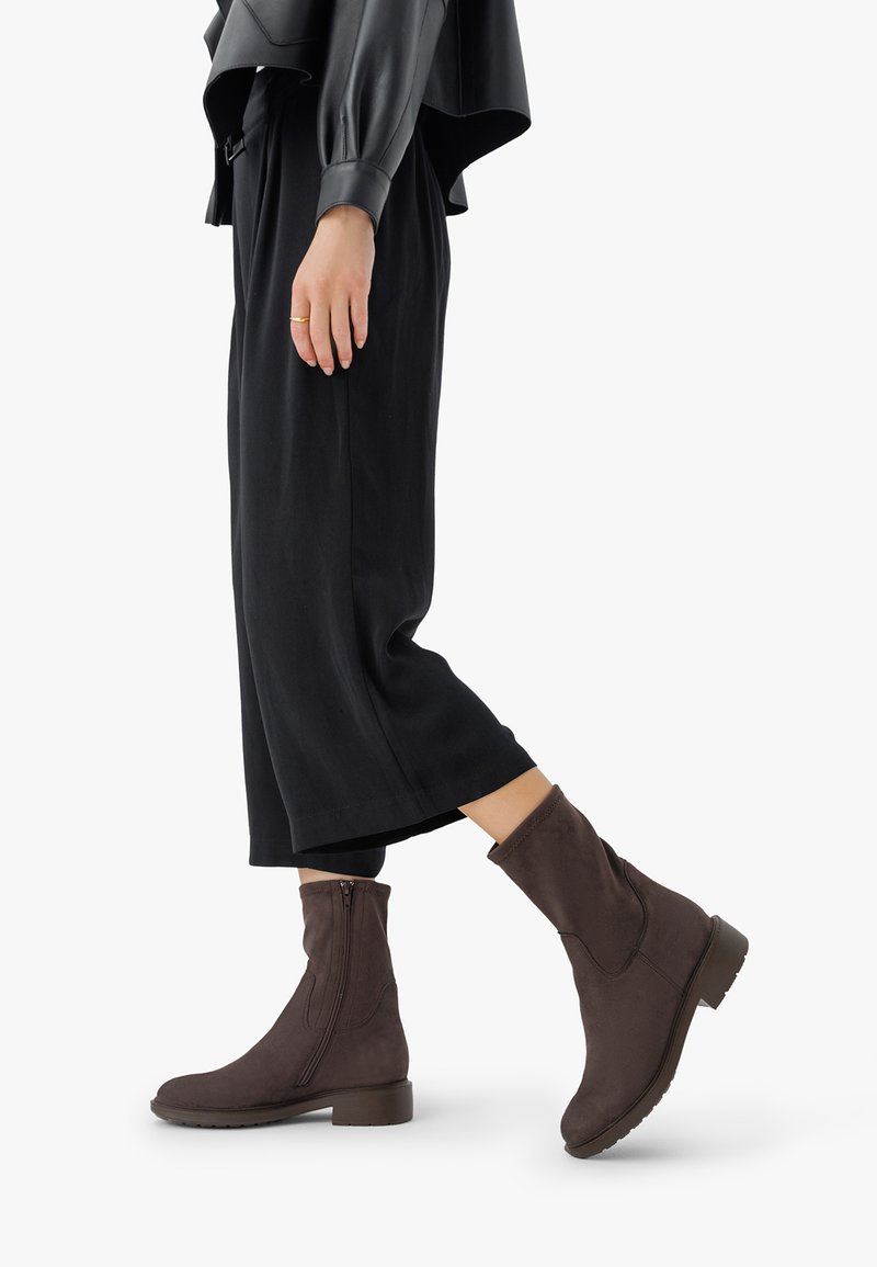 Botine maro din suede, cu fermoar pe lateral, toc mic și vârf rotund. Purtați cu pantaloni negri largi pentru un look relaxat.