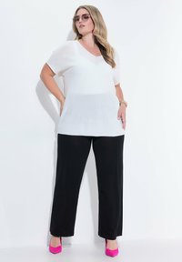 Bílý oversize top s krátkým rukávem v kombinaci s černými kalhotami s širokými nohavicemi a růžovými lodičkami. Hladká tkanina s uvolněným střihem a designem do V.