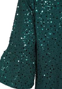 Manche en tissu vert foncé détaillée de petits sequins ronds créant une surface texturée étincelante.