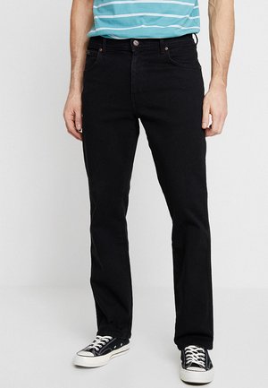 Uomo che indossa jeans neri a gamba dritta, t-shirt blu a righe e sneakers basse nere con lacci bianchi, in piedi su sfondo semplice.