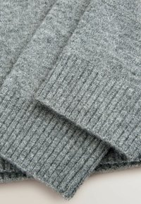 Gros plan sur les manches d'un pull en tricot gris plié avec des poignets côtelés sur un fond clair.