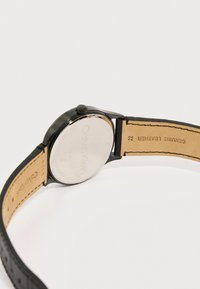 Πίσω όψη ενός ρολογιού χειρός Calvin Klein με μαύρη θήκη και λουράκι από γνήσιο δέρμα που δείχνει τα σήματα της μάρκας και τη ραφή.
