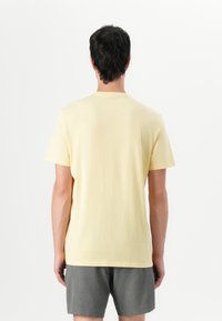 Camiseta de algodón amarilla con mangas cortas y cuello redondo, que presenta un diseño liso y un corte relajado, llevada con pantalones cortos grises.