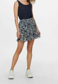 Sukně s květinovým potiskem a volánkovým lemem v námořnické modři a krémové, kombinovaná s tmavým tílkem a bílými teniskami. Sukně je vyrobena z lehkého materiálu.
