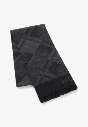 Harmaa huivi, jossa on geometrinen kuvio, valmistettu pehmeästä materiaalista ja hapsut reunoissa. Musta ja tummanharmaa värimaailma, jossa hienovarainen brändäys.