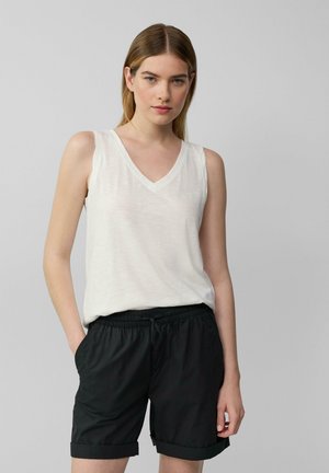 Witte mouwloze v-hals top gecombineerd met zwarte shorts met elastische tailleband, voorzien van cuffs en zijzakken, weergegeven tegen een neutrale achtergrond.