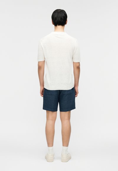 Ανοιχτό γκρι πουκάμισο με κοντά μανίκια, σκούρο μπλε σορτς, λευκά αθλητικά παπούτσια, με λεία υφή· το πουκάμισο φτάνει λίγο κάτω από τη μέση, το σορτς έχει δύο πίσω τσέπες.