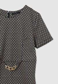 Robe à manches courtes à motif bleu marine et crème, présentant un design géométrique avec un accent de chaîne dorée à la taille.