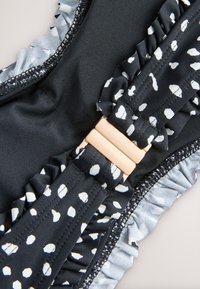 Mustast ujumisriide kangast valgete täppidega, krakitud detailide ja metallik roosakuldsete kinnitusdetailidega. Sile tekstuur helesiniste kontrastsete äärtega.