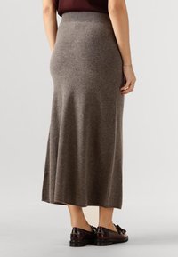 Long, brown knit skirt with a fitted waistband, flowing design, and soft texture. Paired with dark slip-on shoes.