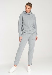 Szary, miękki hoodie z kapturem i luźnym krojem, w zestawie z dopasowanymi spodniami o zwężanym kroju, wyposażonymi w boczne kieszenie i detal w postaci wiązania w talii.