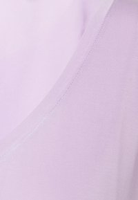 Ljus lavendelfärgad linne med en jämn textur, djup V-ringning och fin sömnad längs kanterna för en sömlös finish.