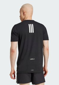 Svart idretts T-skjorte med korte ermer. Har tre hvite vertikale striper på baksiden og "LES MILLS" merke nær sømmen.