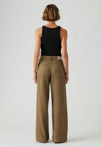 Pantalones de pierna ancha en tela verde oliva, con una cintura alta y bolsas traseras. Combinados con una camiseta negra ajustada.