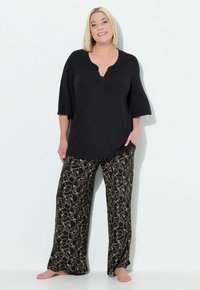 Zwarte top met korte mouwen en een V-hals, gecombineerd met loszittende zwarte broek met een abstract goudkleurig patroon. Gladde stof, casual ontwerp.