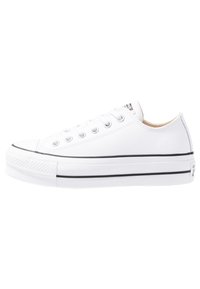 Zapatilla de lona blanca con suela de goma negra, punta redonda y cinco ojales. Presenta costuras texturizadas y una etiqueta en el talón con la marca.
