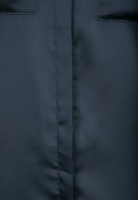 Námorně modrá látka s hladkým povrchem, se dvěma náprsními kapsami nahoře a středovým švem, vhodná pro venkovní nošení.